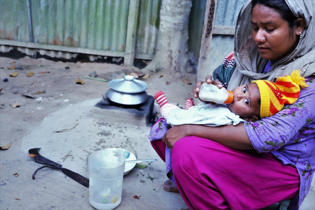 A mother tenderly feeds her baby outdoors in Gazipur, Bangladesh, capturing a moment of care and love.